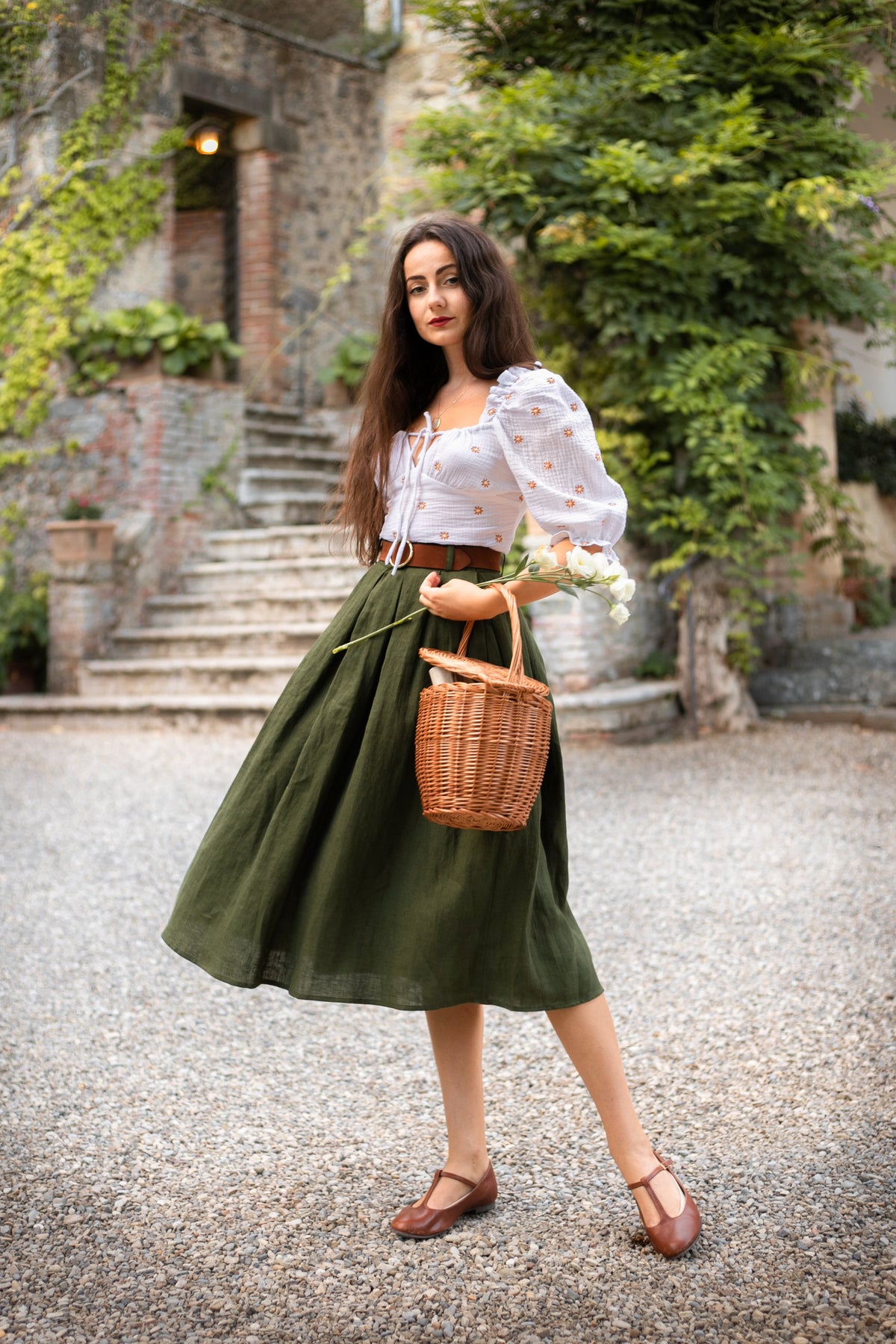 Ivy moss green pleated linen midi skirt in motion, holding a wicker basket