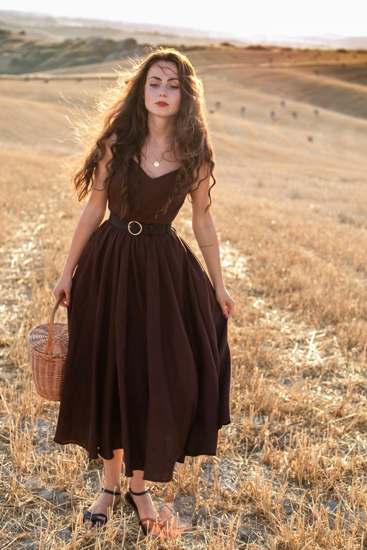 Andalusia dark brown linen dress with a full gathered skirt and black belt in a Tuscan field at golden hour