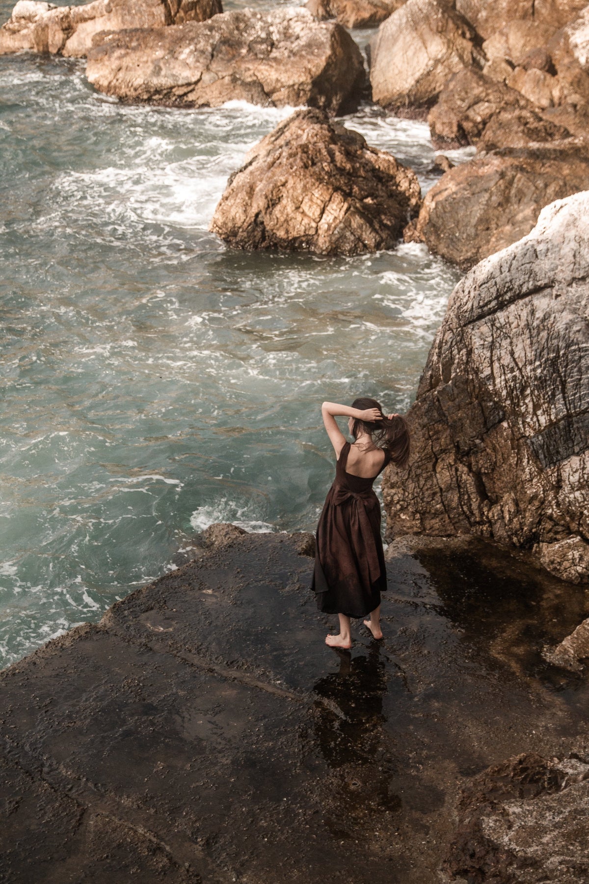 Andalusia dark brown linen dress with a dramatic full skirt photographed among coastal rocks