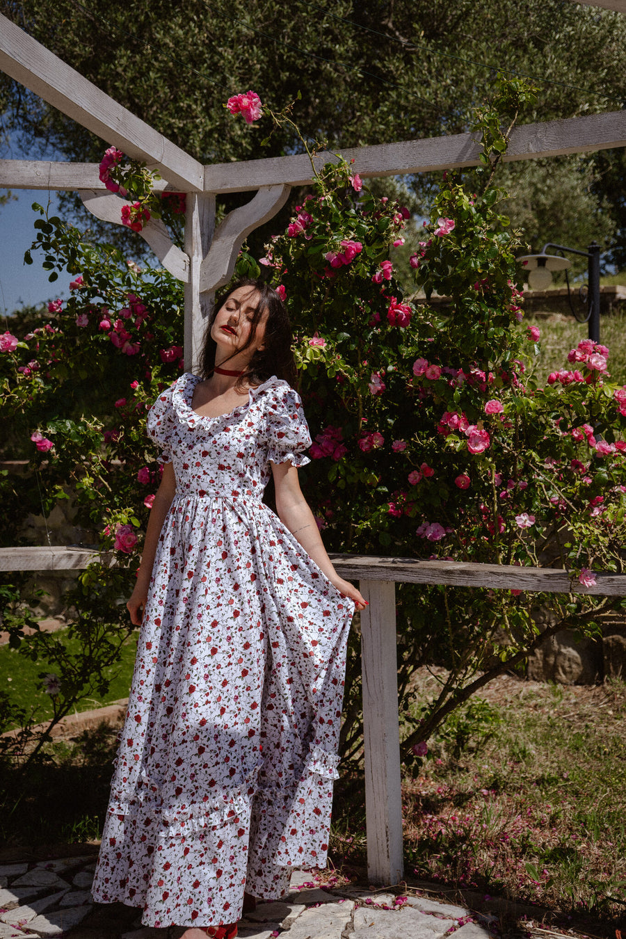 Vittoria white cotton maxi dress with a red rose print and puff sleeves under a rose pergola