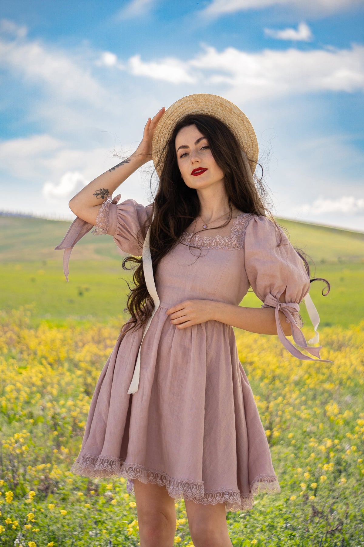April antique pink linen mini dress with bows at the sleeves, worn with a straw hat in a flower meadow