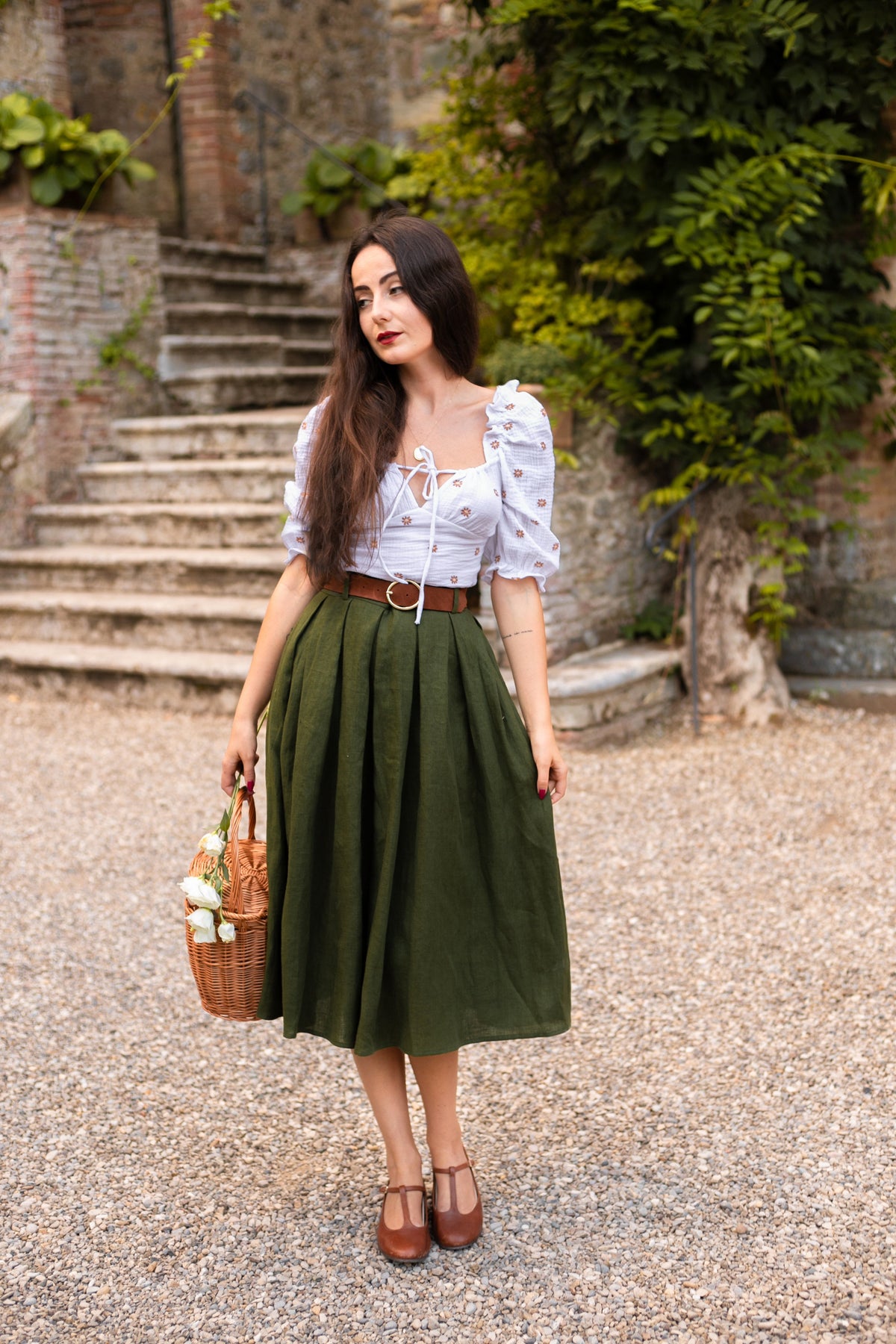 Ivy moss green pleated linen midi skirt with a white blouse, standing by old stone steps