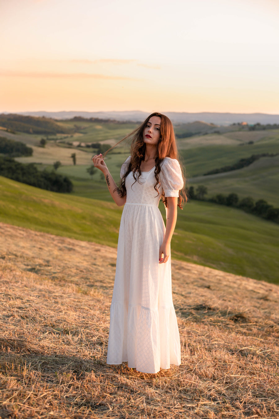Ophelia white cotton Victorian-inspired wedding dress, standing on a hillside at sunset