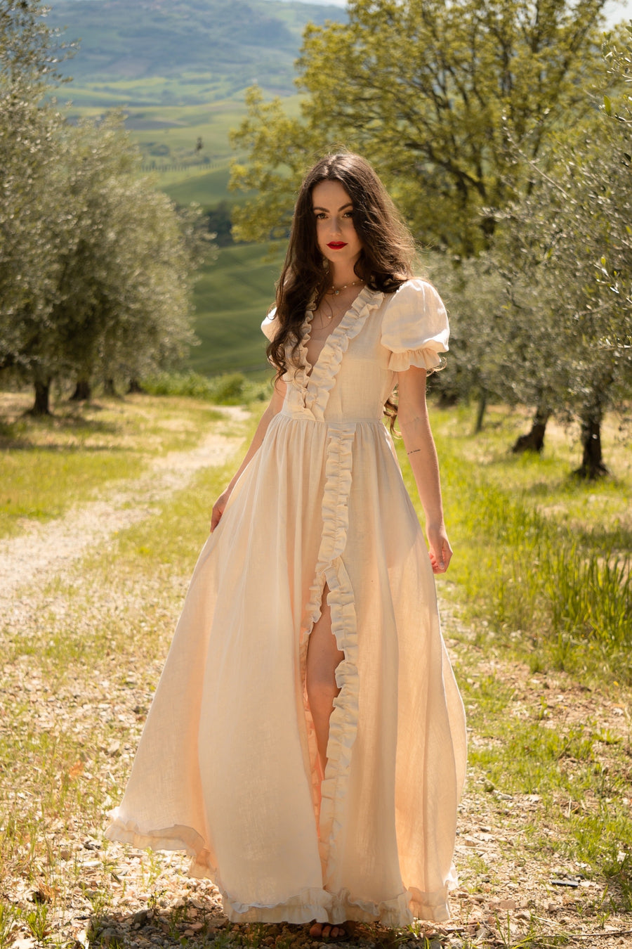 Celeste cream linen wedding dress with puff sleeves and a ruffled V-neckline on a path through an olive grove