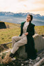 Woman in a green coat sitting on a rock with mountains in the background