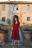 Three-quarter view of the Siena burgundy linen midi dress in an elegant Italian courtyard