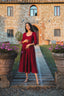 Full-length view of the Siena burgundy linen midi dress in front of a rustic stone villa
